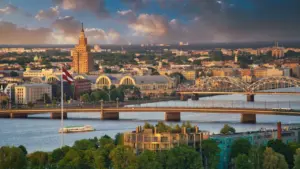 Panorāmas skats uz Rīgas vēsturisko centru un Daugavu saulainā dienā.