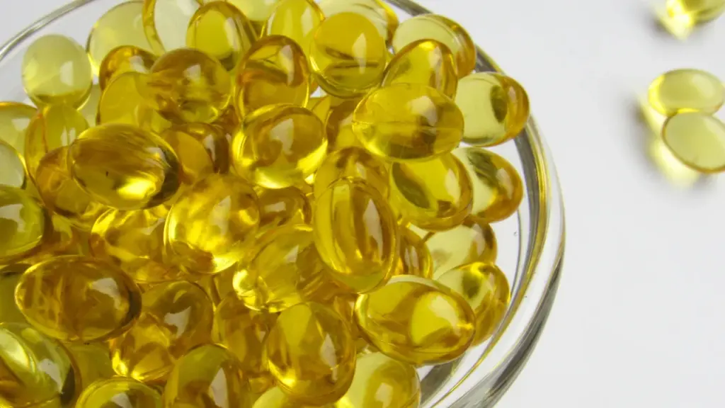 Dzeltenas D vitamīna kapsulas stikla traukā uz gaišas virsmas, tuvu uzņemts kadrs.