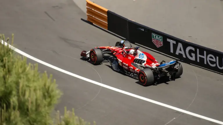 Sarkana Formula 1 formula sacīkšu auto izbrauc cauri asam trases līkumam saulainā dienā.