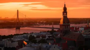 Panorāmas skats uz Rīgas siluetu saulrieta gaismā pāri Daugavai un Vanšu tiltam.