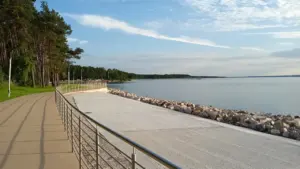 Modernā gājēju promenāde gar ezeru ar gludu segumu un metāla margām.